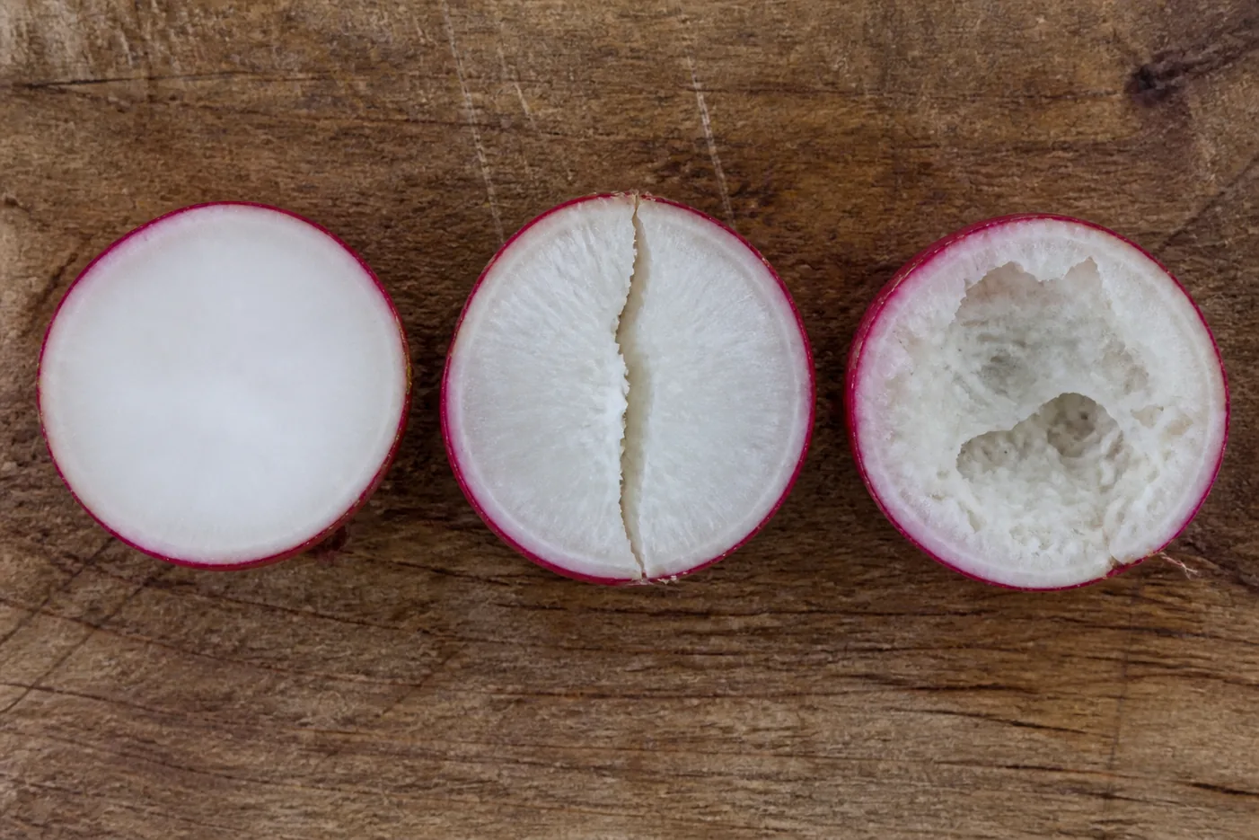 Three radish roots cut in half showing a solid crisp white interior, one split through the flesh, and one dry and spongy inside