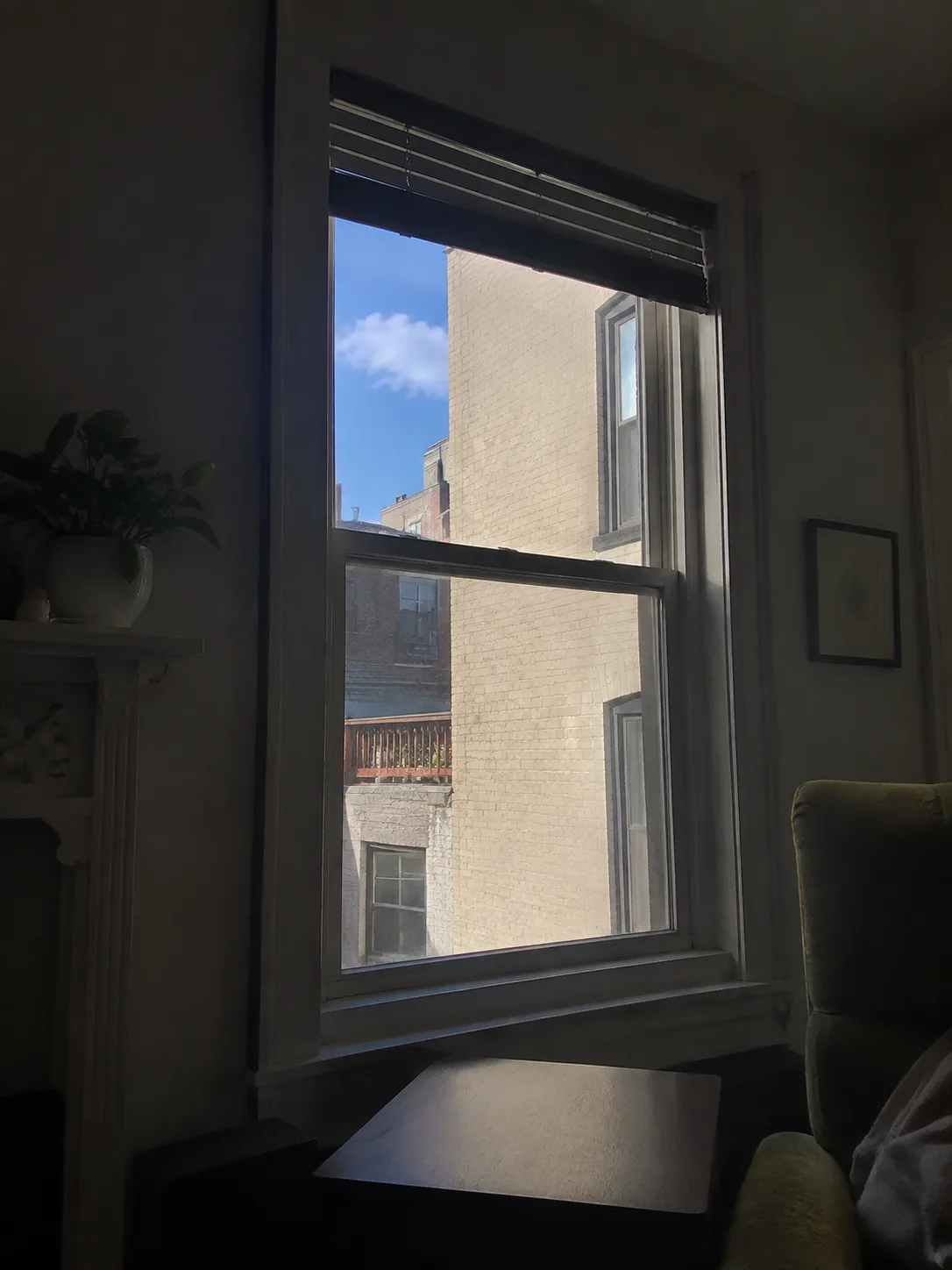 The view outward from where a plant would stand in a dim room, a patch of blue sky and a brightly sunlit wall visible through the window while the room itself stays shadowed